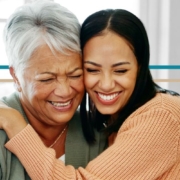 A young woman hugs an older woman while both are smiling