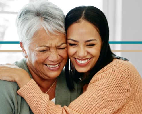 A young woman hugs an older woman while both are smiling