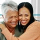 A young woman hugs an older woman while both are smiling