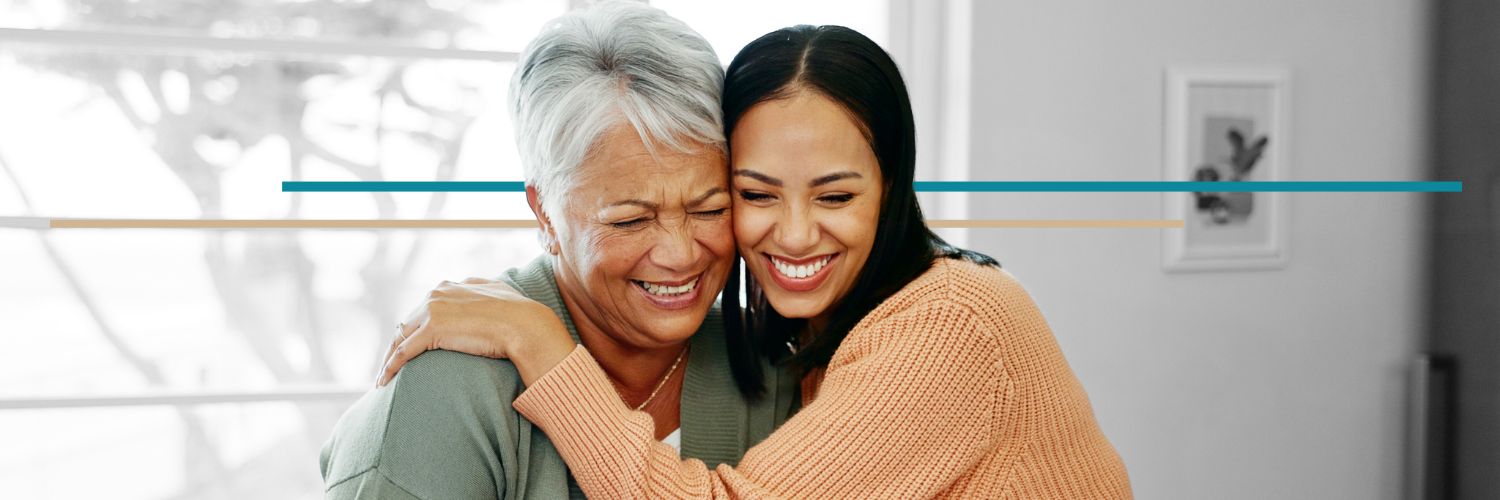 A young woman hugs an older woman while both are smiling