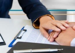 A woman in a suit jacket puts her hand over the hand of another person soothingly