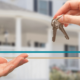 hands exchanging keys to a home in the background