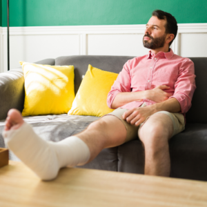 man sitting on a couch with a leg in a cast and crutches beside him