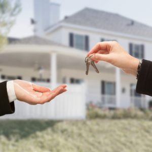 women's hands exchanging keys with a home in the background