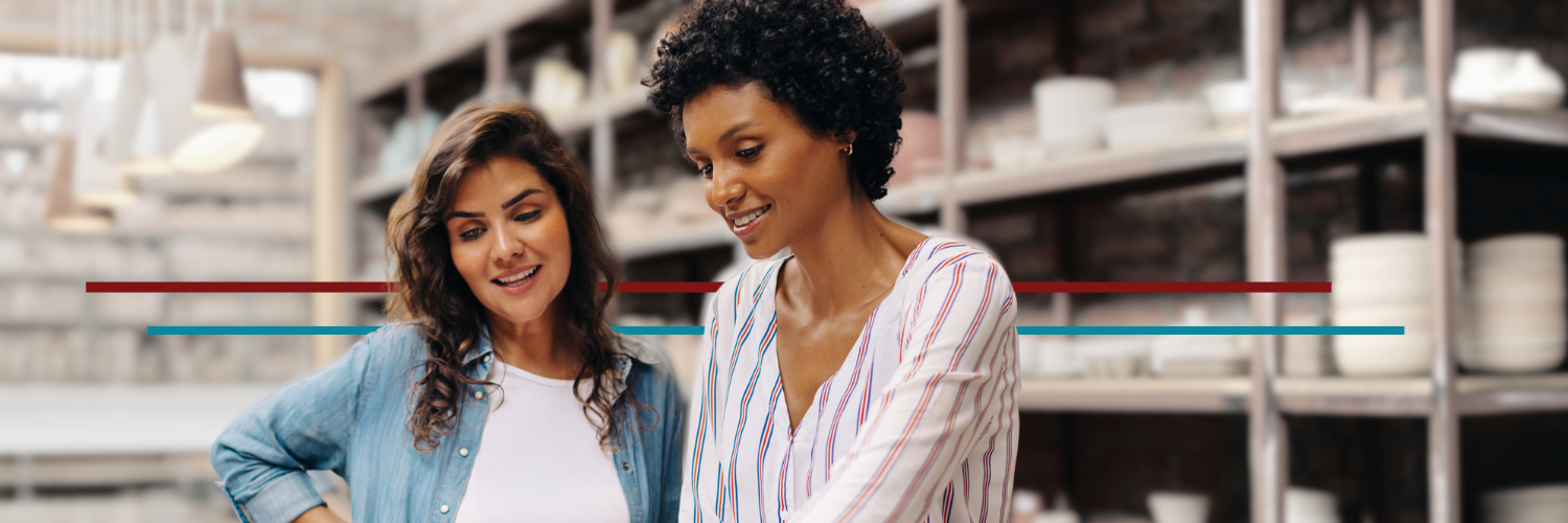 two women in their 30s in their business smiling and discussing business looking at a laptop
