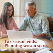 middle aged couple at kitchen table scattered with papers and looking at laptop