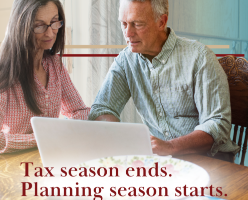 middle aged couple at kitchen table scattered with papers and looking at laptop