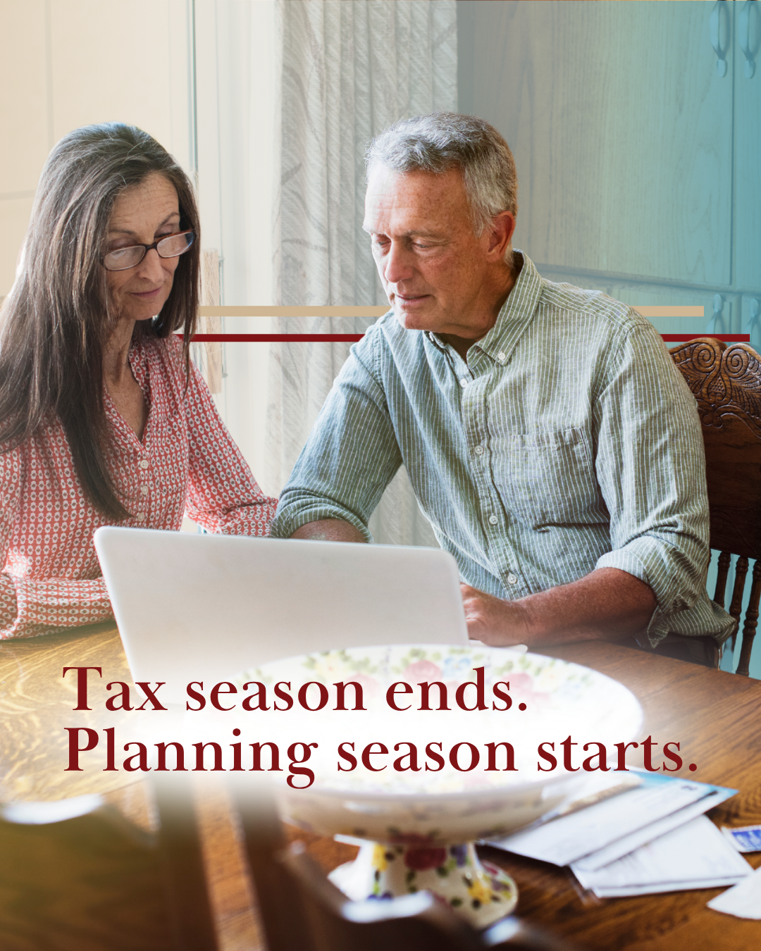 middle aged couple at kitchen table scattered with papers and looking at laptop