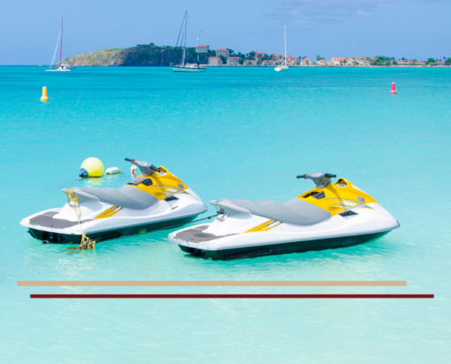 2 unoccupied jet ski parked in a shallow boat harbor with sailboats in the distance