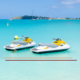 2 unoccupied jet ski parked in a shallow boat harbor with sailboats in the distance